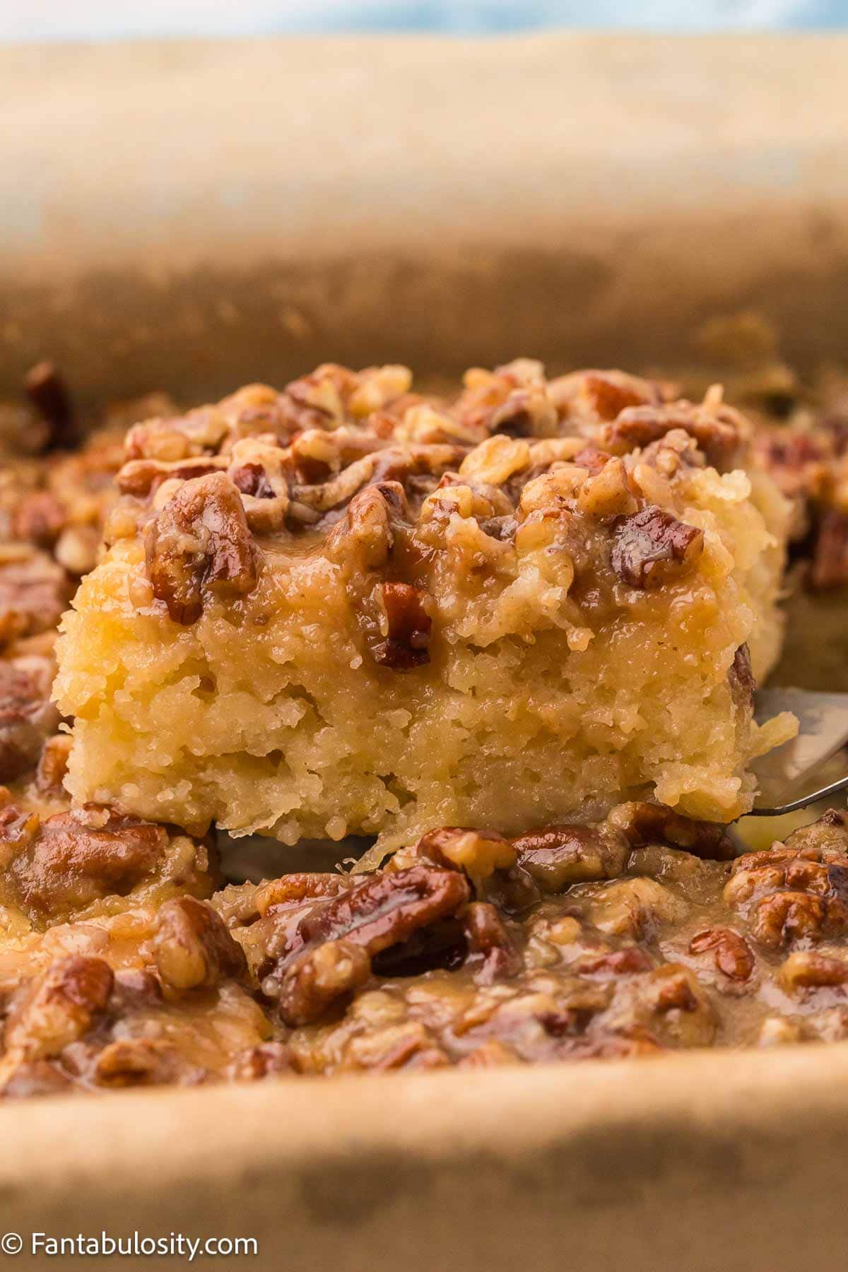 Square of granny cake with brown sugar pecan topping being lifted from the pan.