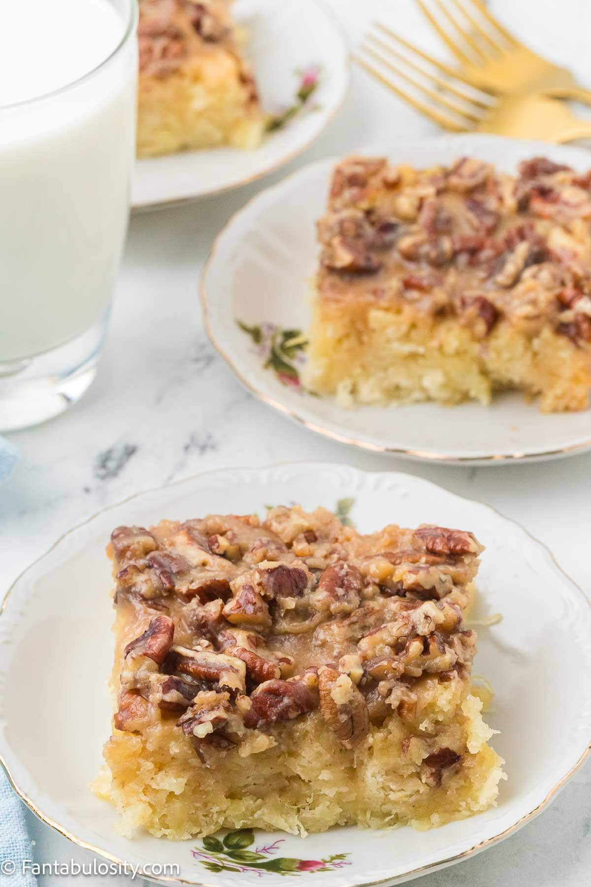 Slices of granny cake on plates with a glass of milk and gold forks.