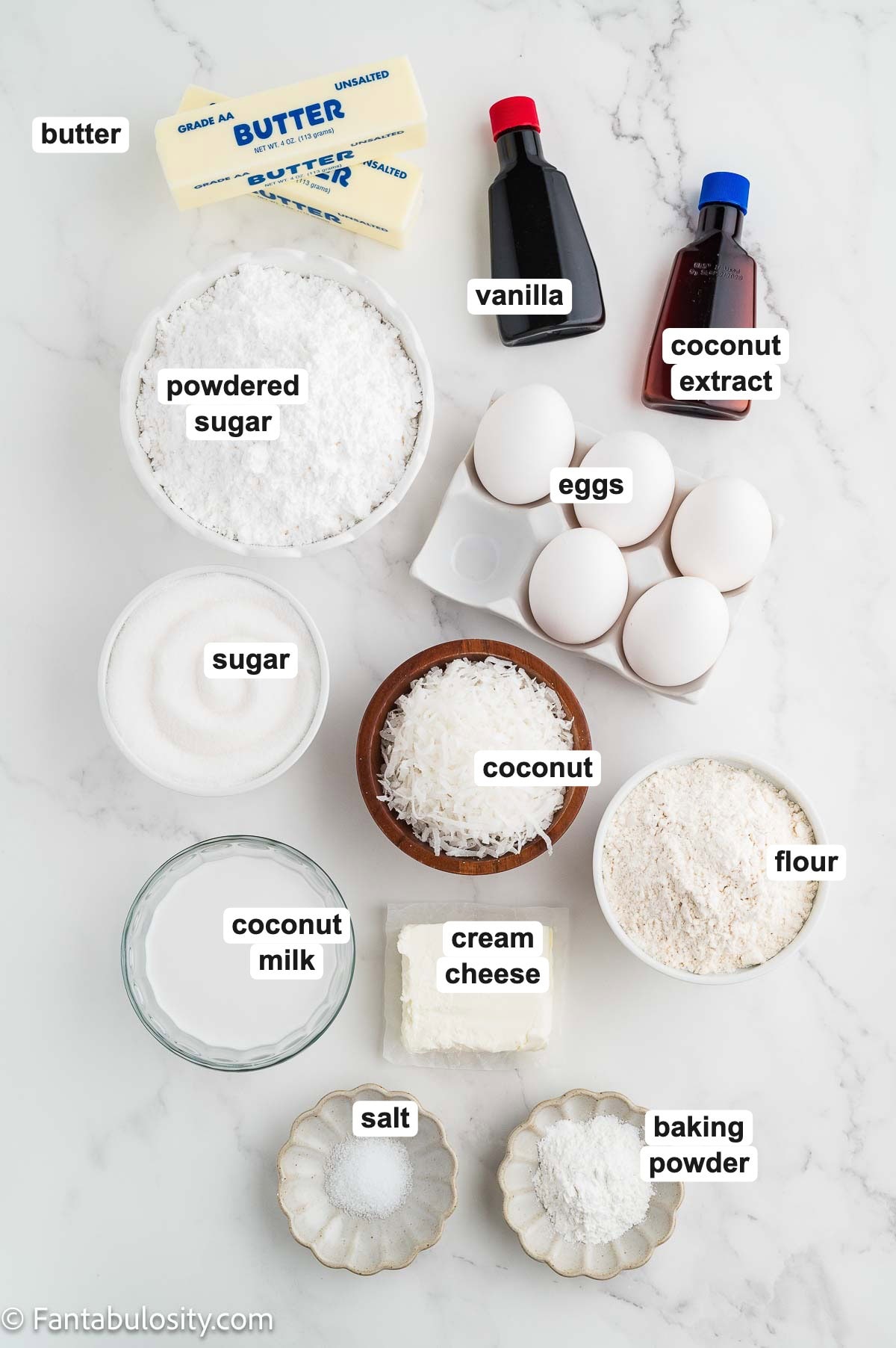 Labeled ingredients to make coconut sheet cake, including flour, sugar, powdered sugar, butter, eggs, coconut milk, shredded coconut, cream cheese, vanilla, and coconut extract.
