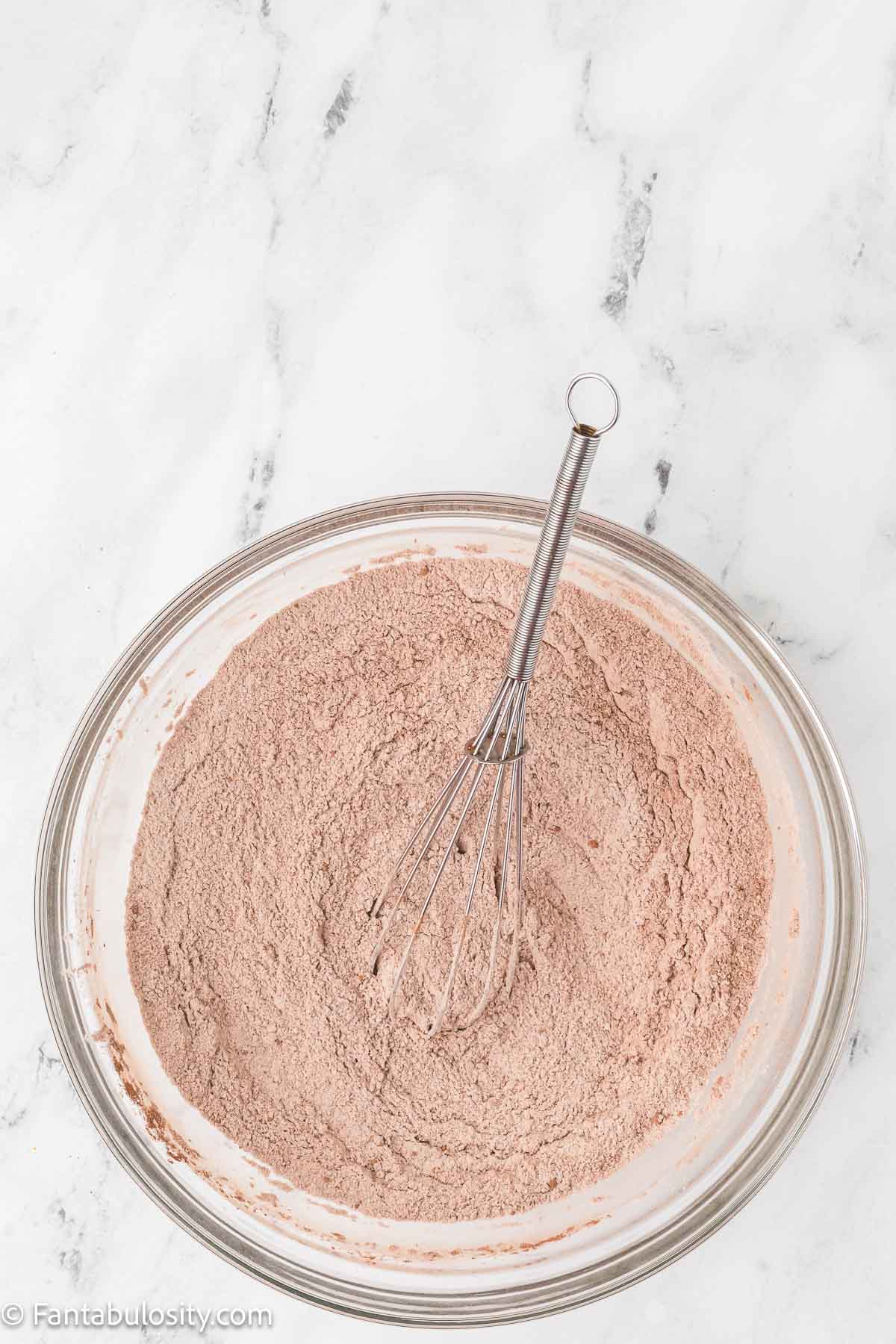 Flour, sugar, cocoa, and other dry cake ingredients whisked together in a glass bowl.