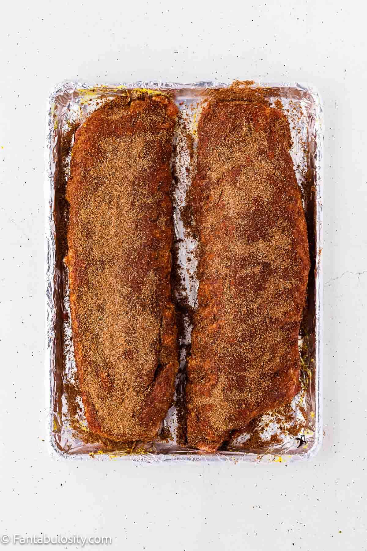 Two racks of ribs coated in a thick layer of homemade dry rub on a sheet pan