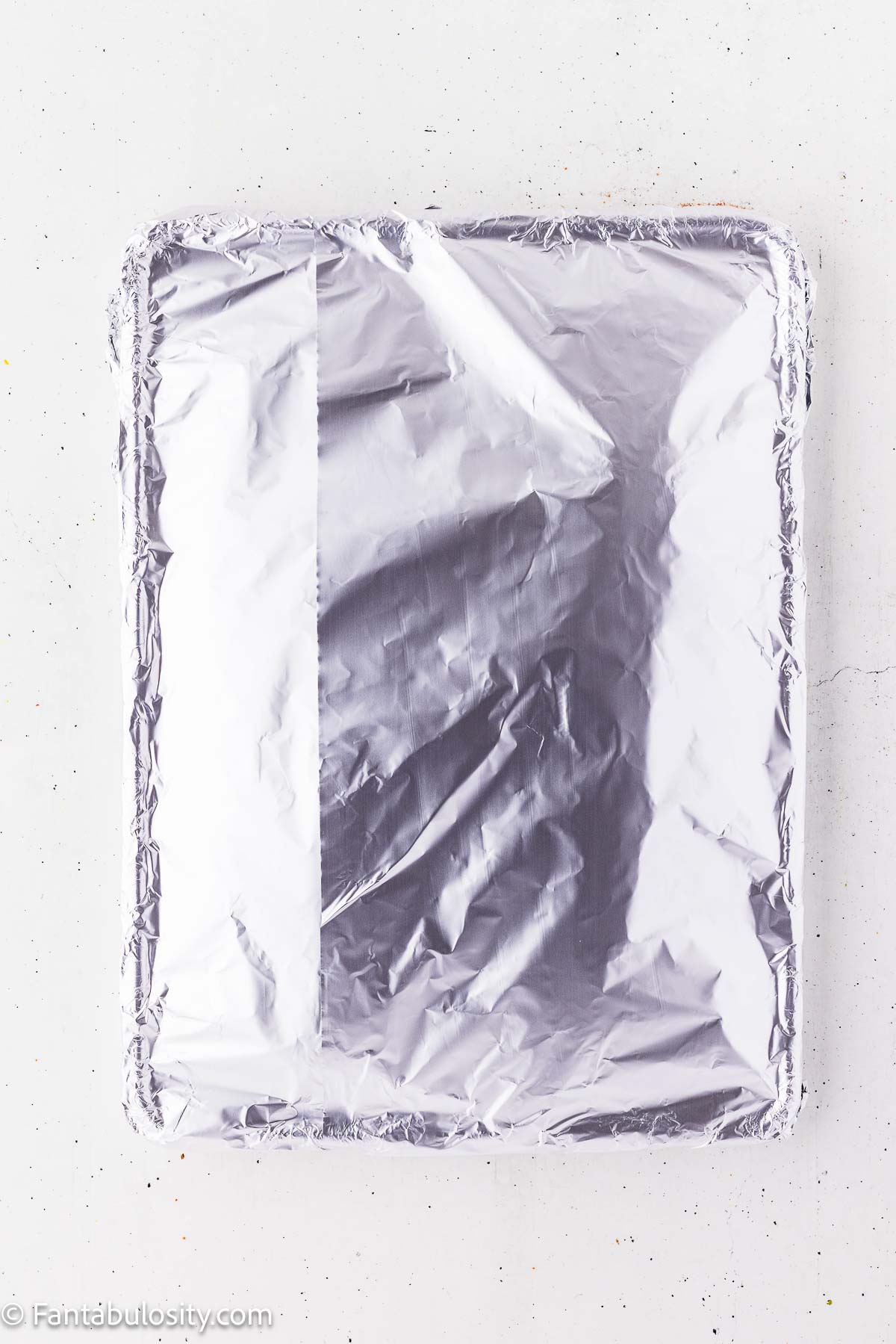 Sheet pan of seasoned ribs covered tightly with heavy-duty aluminum foil