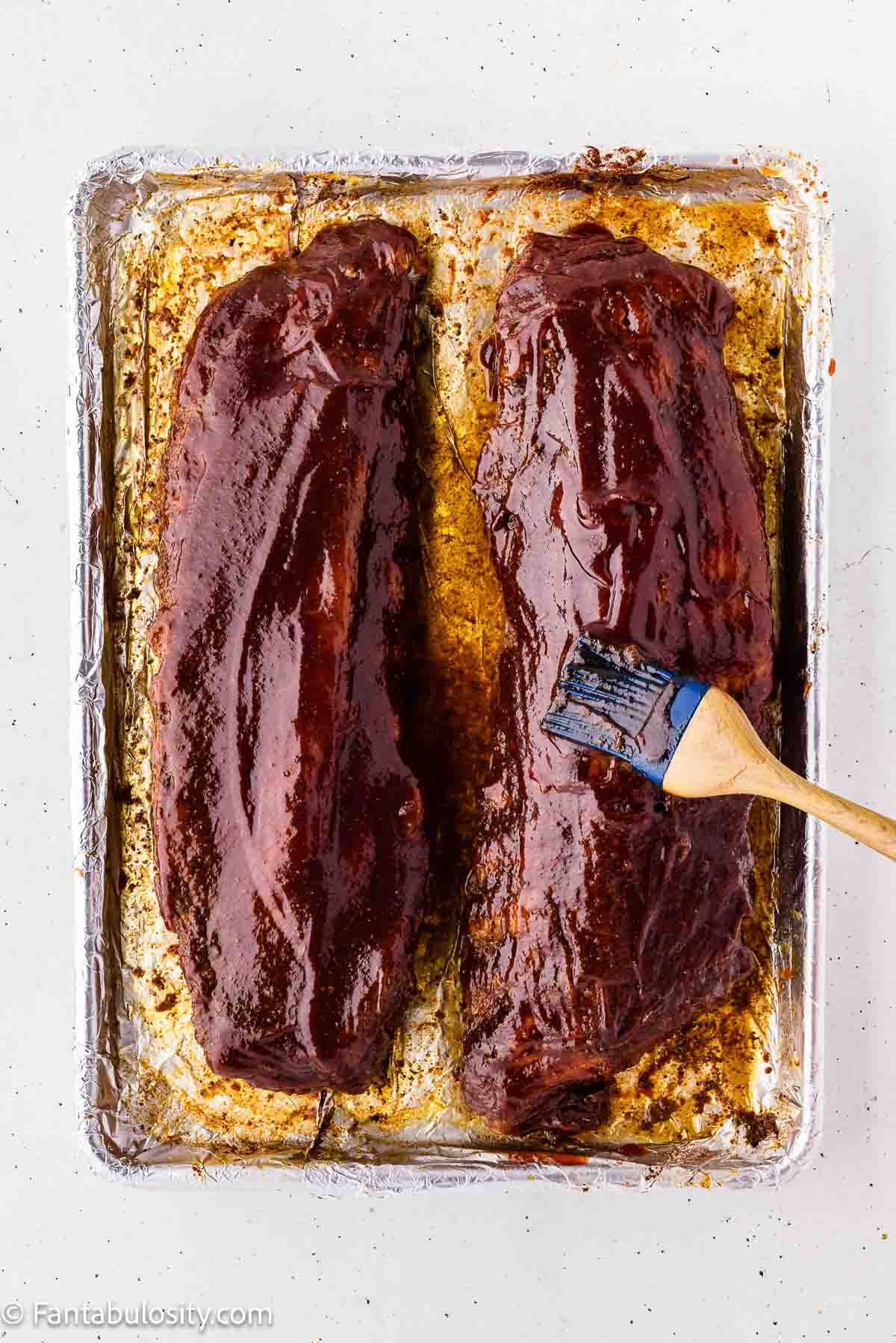 Brushing BBQ sauce over baked ribs before the final uncovered bake