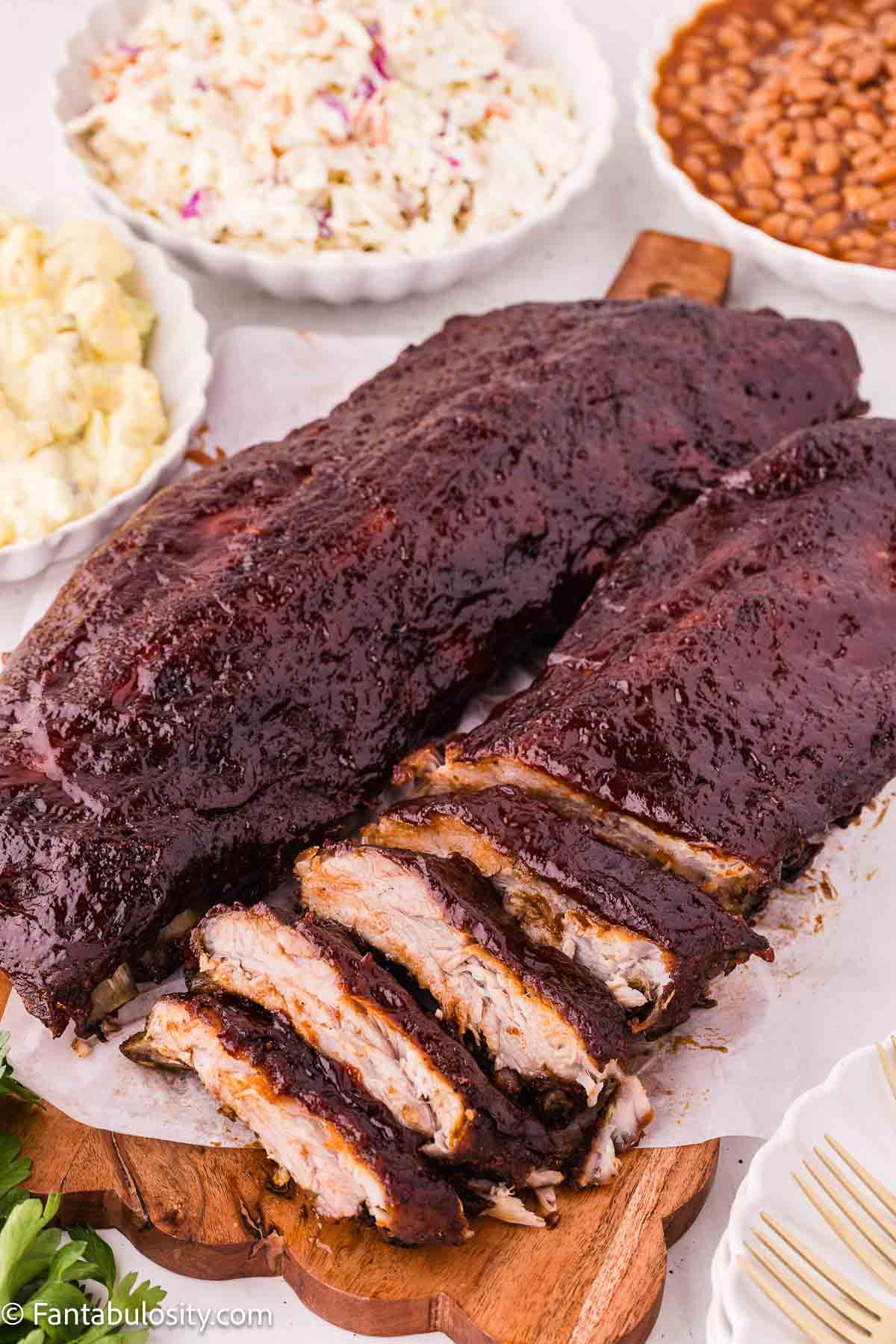 Two racks of glazed oven baked ribs beside bowls of classic cookout sides