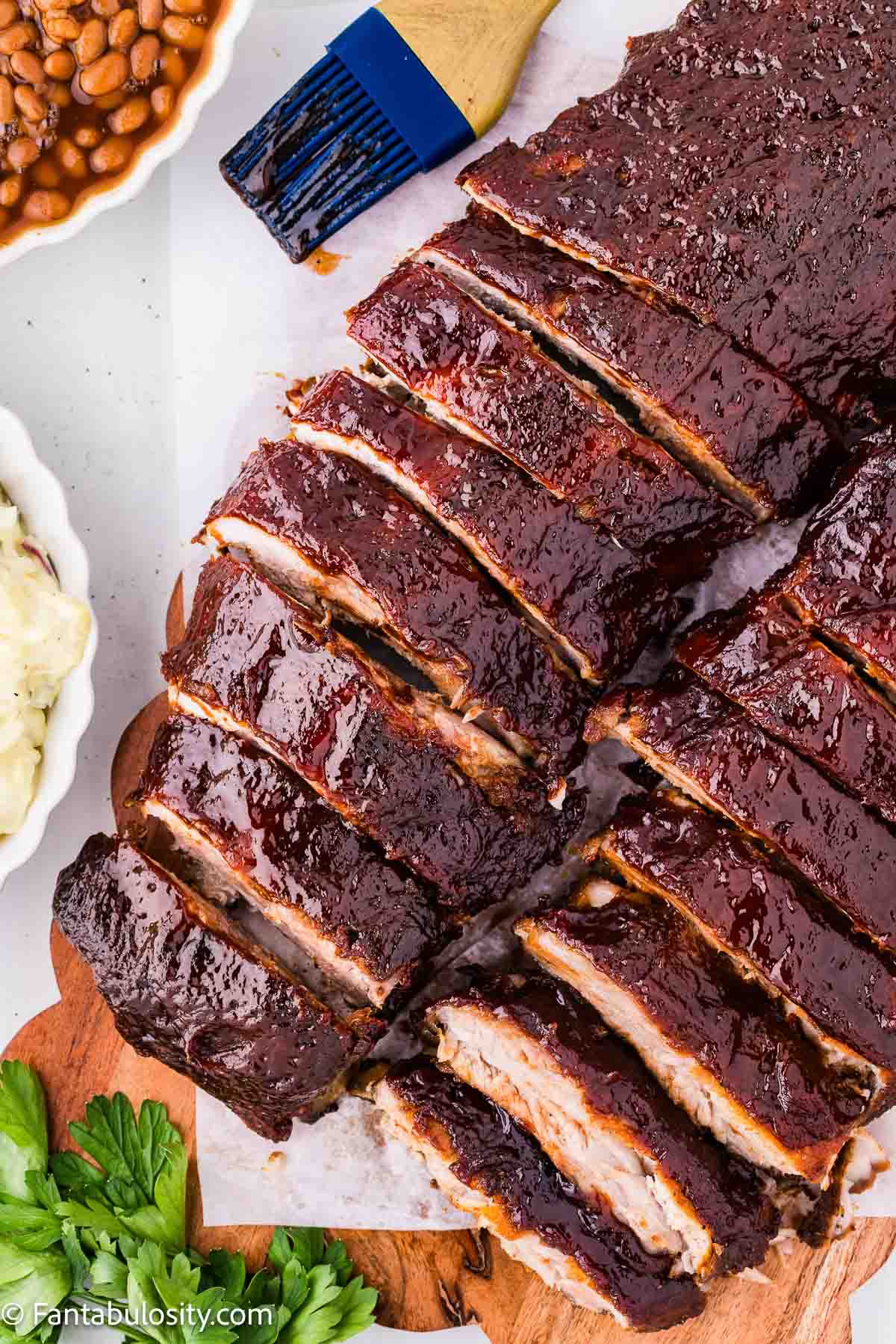 Sliced oven baked ribs on a board with cookout sides in the background