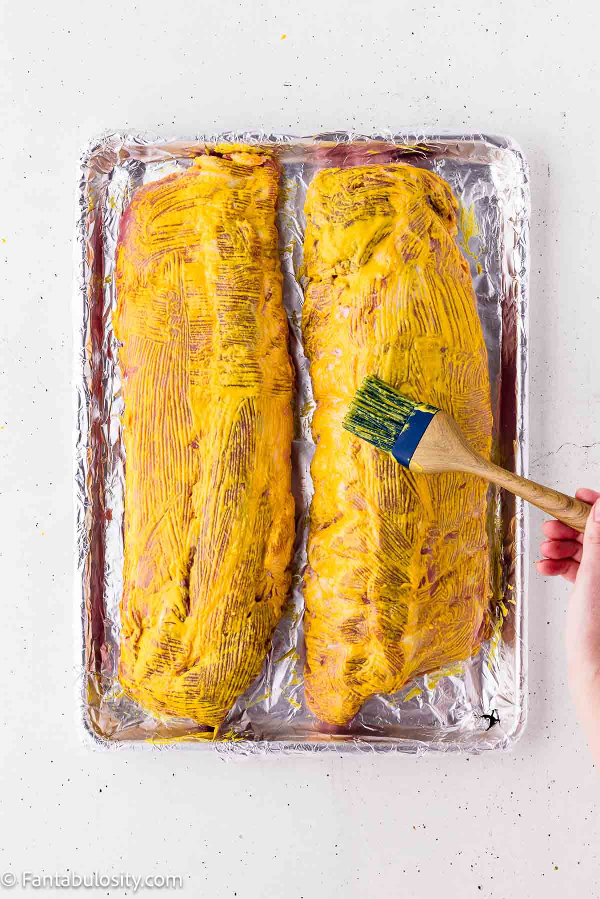 Brushing yellow mustard over baby back ribs as a binder for the dry rub