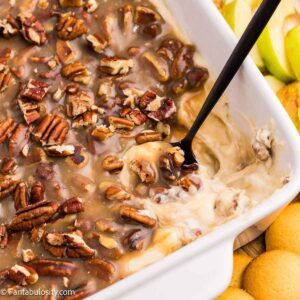 Close-up of pecan pie dip with a spoon showing the creamy base beneath the pecan topping.