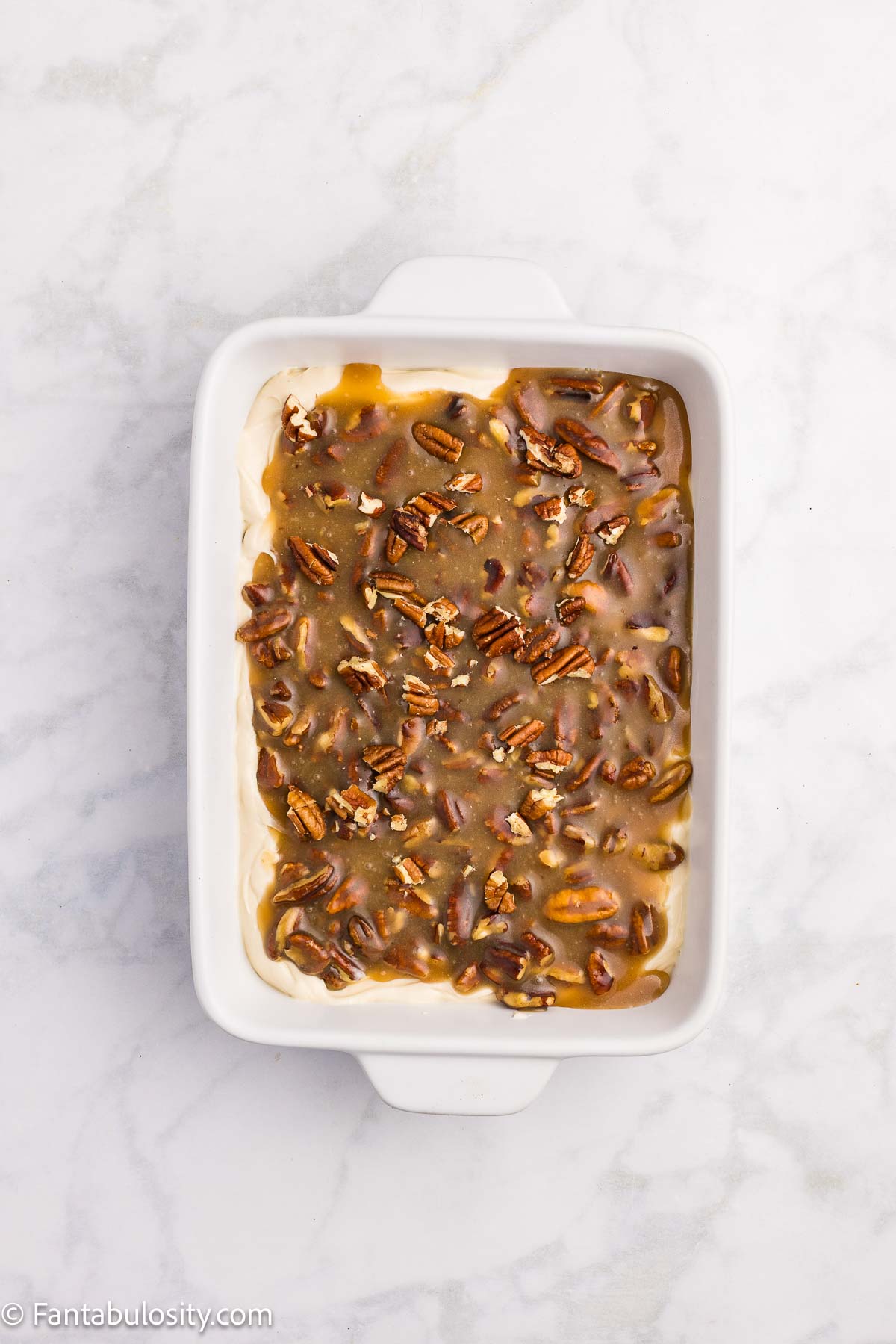 Pecan topping spread over the cream cheese layer in a white rectangular dish.