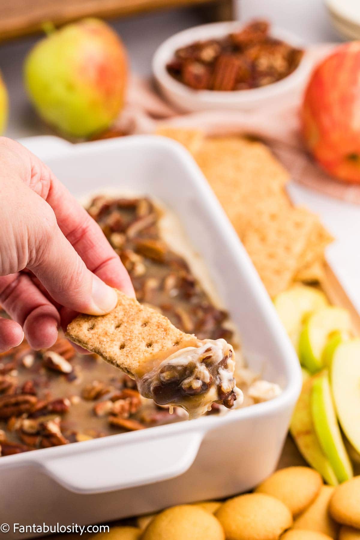 Graham cracker scooping cream cheese and pecan topping from a dish of pecan pie dip.