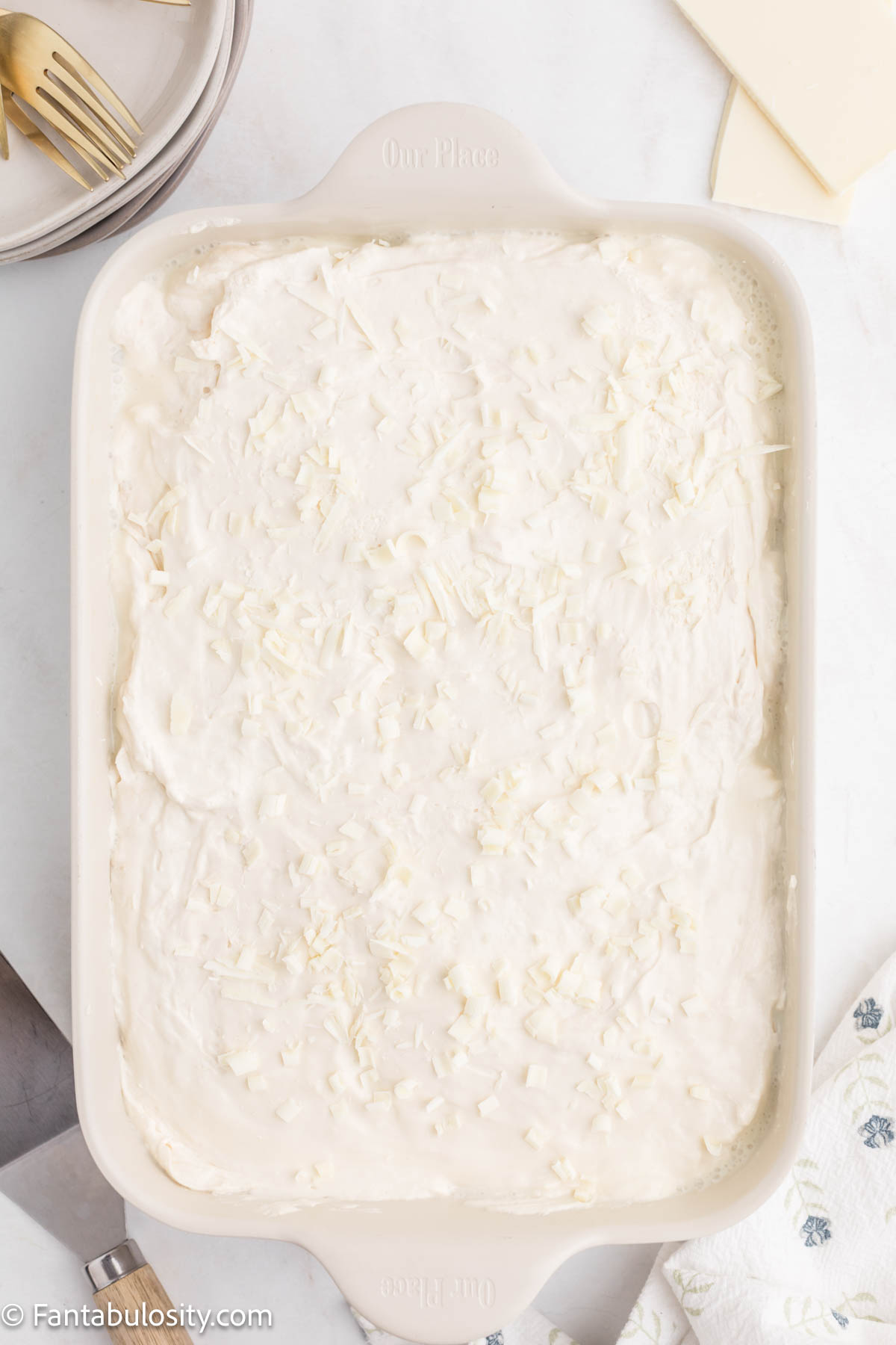 Red velvet poke cake frosted in the pan and topped with white chocolate shavings.