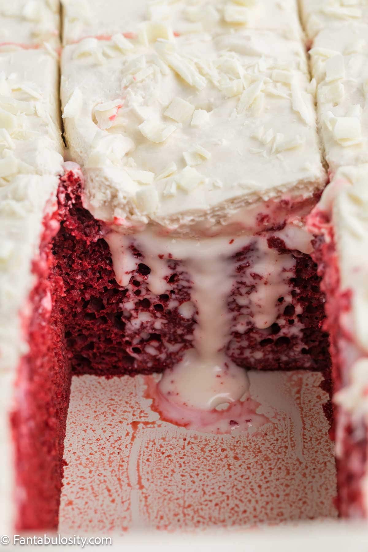 A slice of red velvet poke cake lifted out of the pan with filling running down the side.