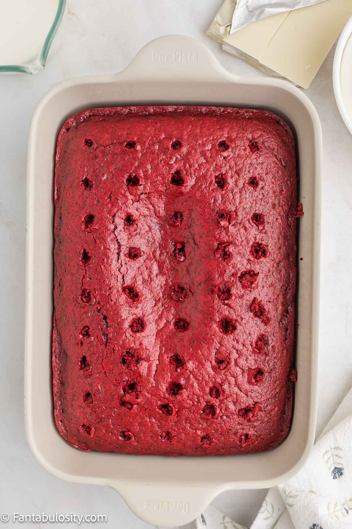 A baked red velvet cake in a 9x13 pan poked full of holes with a skewer.