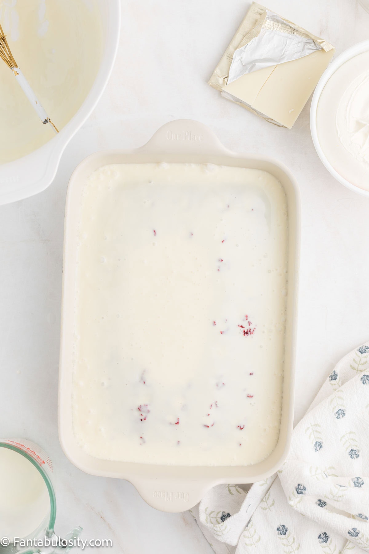 The sweetened condensed milk filling poured over the poked red velvet cake in the pan.