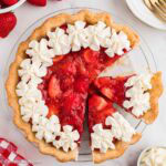 Fresh strawberry pie with whipped cream around the edge and a slice pulled away.