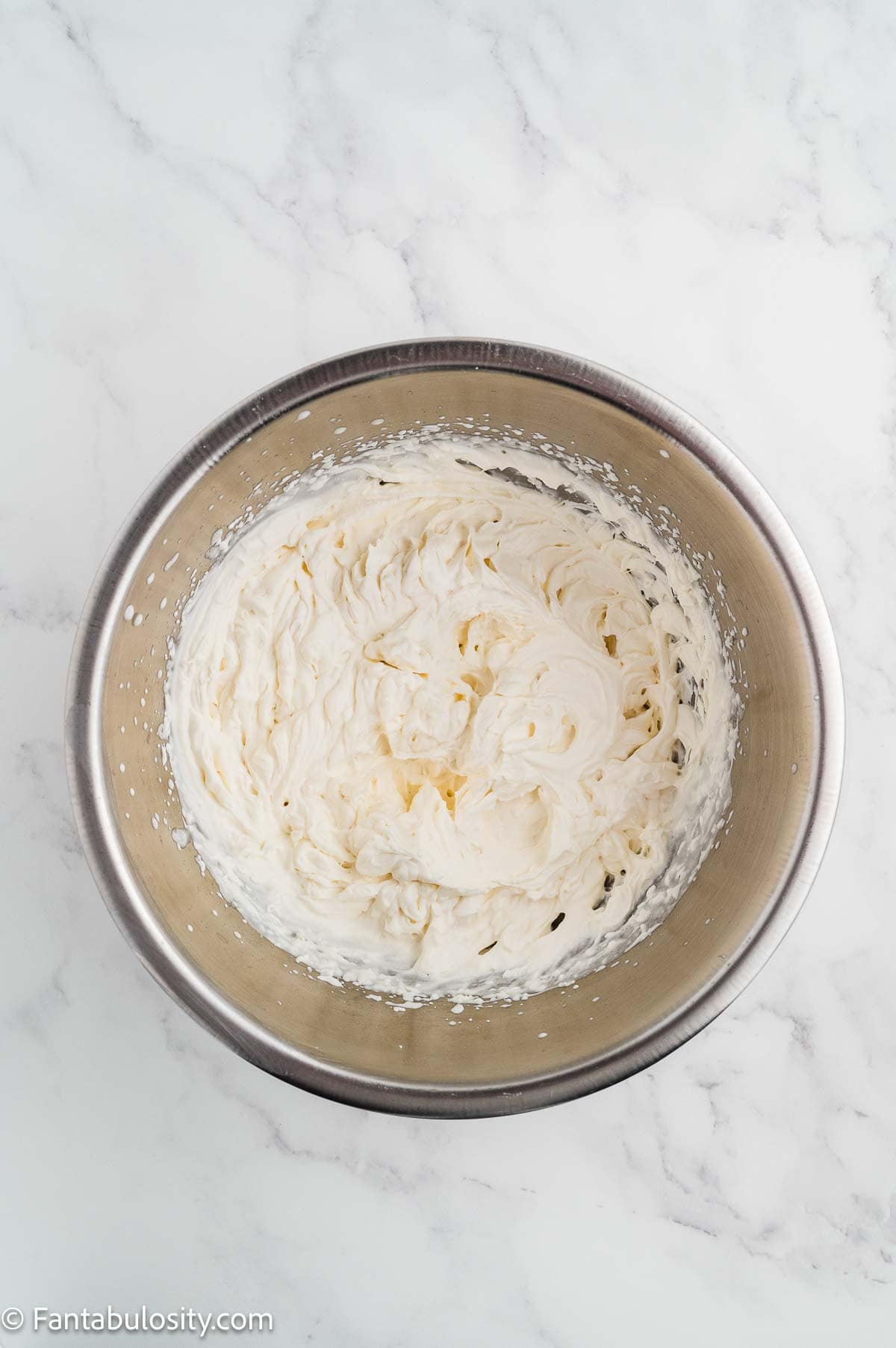 Whipped cream beaten to stiff peaks in a metal bowl.
