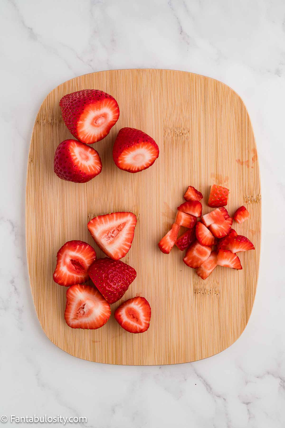 Halved and diced strawberries on a wooden cutting board.