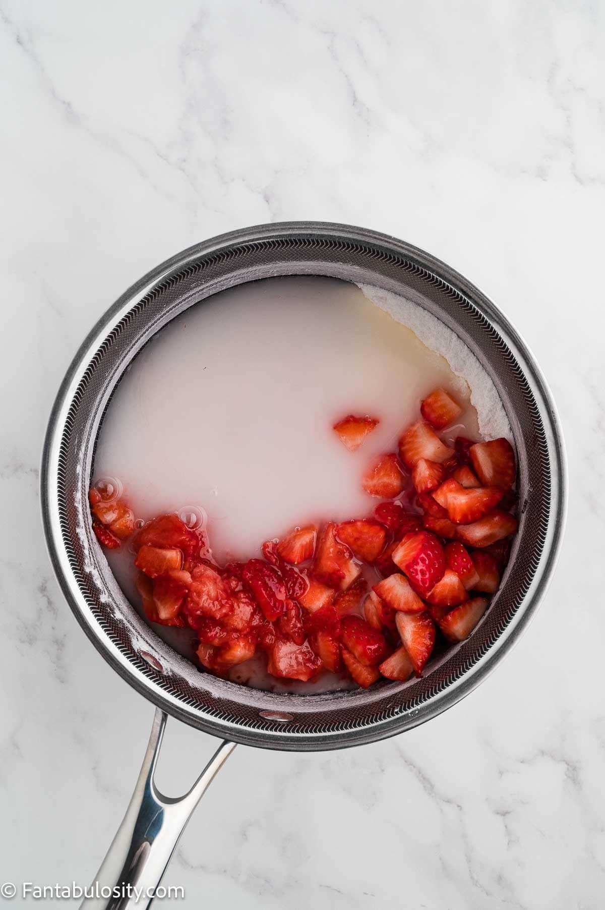 Diced strawberries and water added to the sugar mixture in a saucepan.