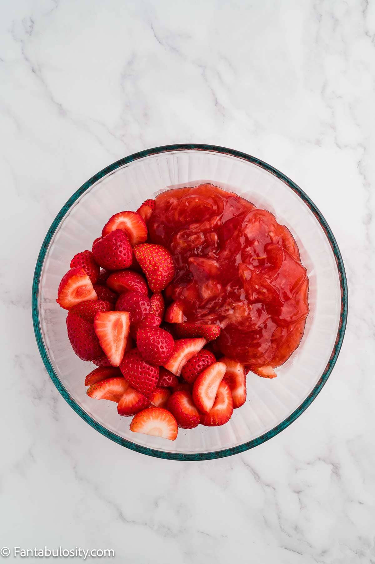 Halved strawberries stirred into strawberry glaze in a glass bowl.