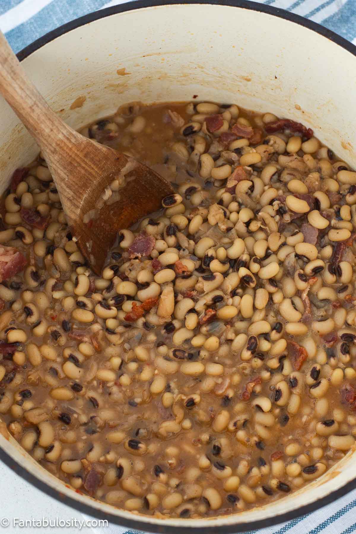 Cooked black eyed peas and broth in a Dutch oven with a wooden spoon.
