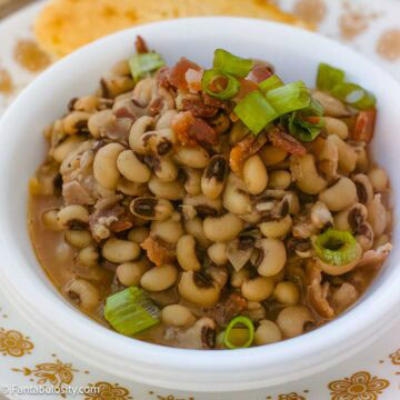 Black eyed peas with bacon and sliced green onions in a white bowl.