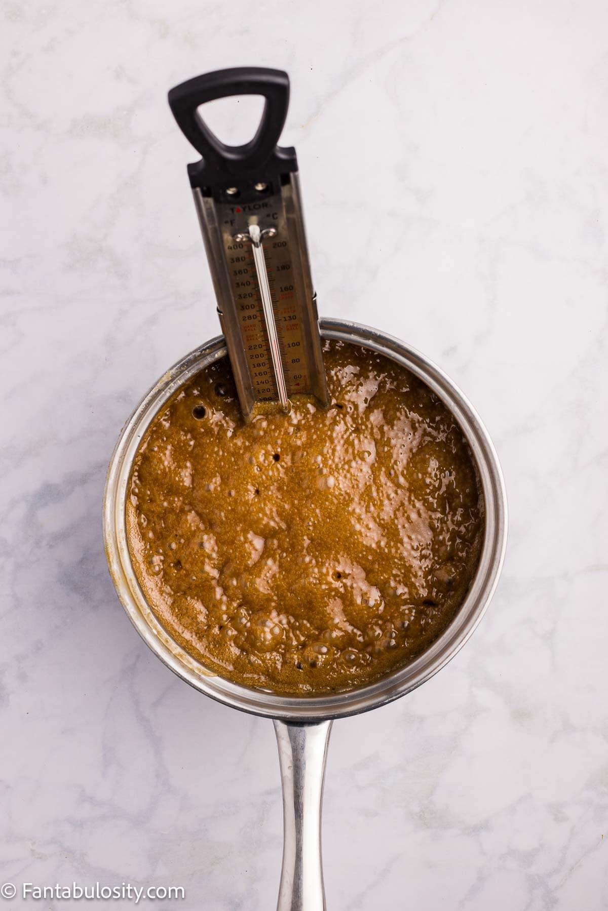 Brown sugar fudge mixture boiling in a saucepan fitted with a candy thermometer.