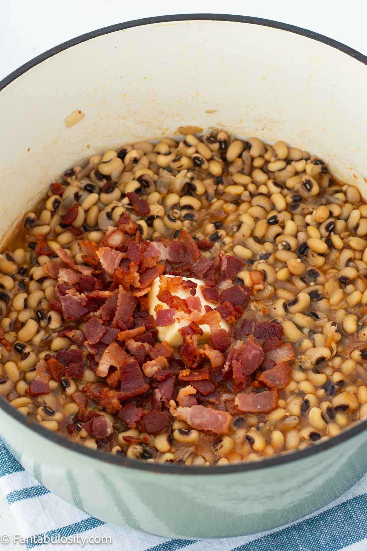 Butter and cooked bacon added to black eyed peas in a Dutch oven.