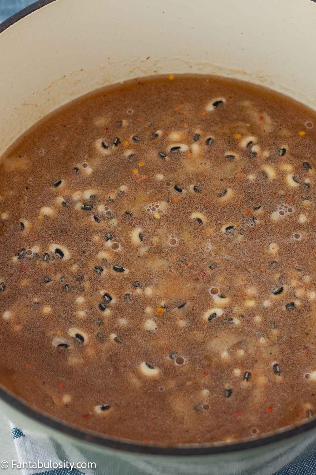 Black eyed peas bubbling in seasoned broth in a Dutch oven.