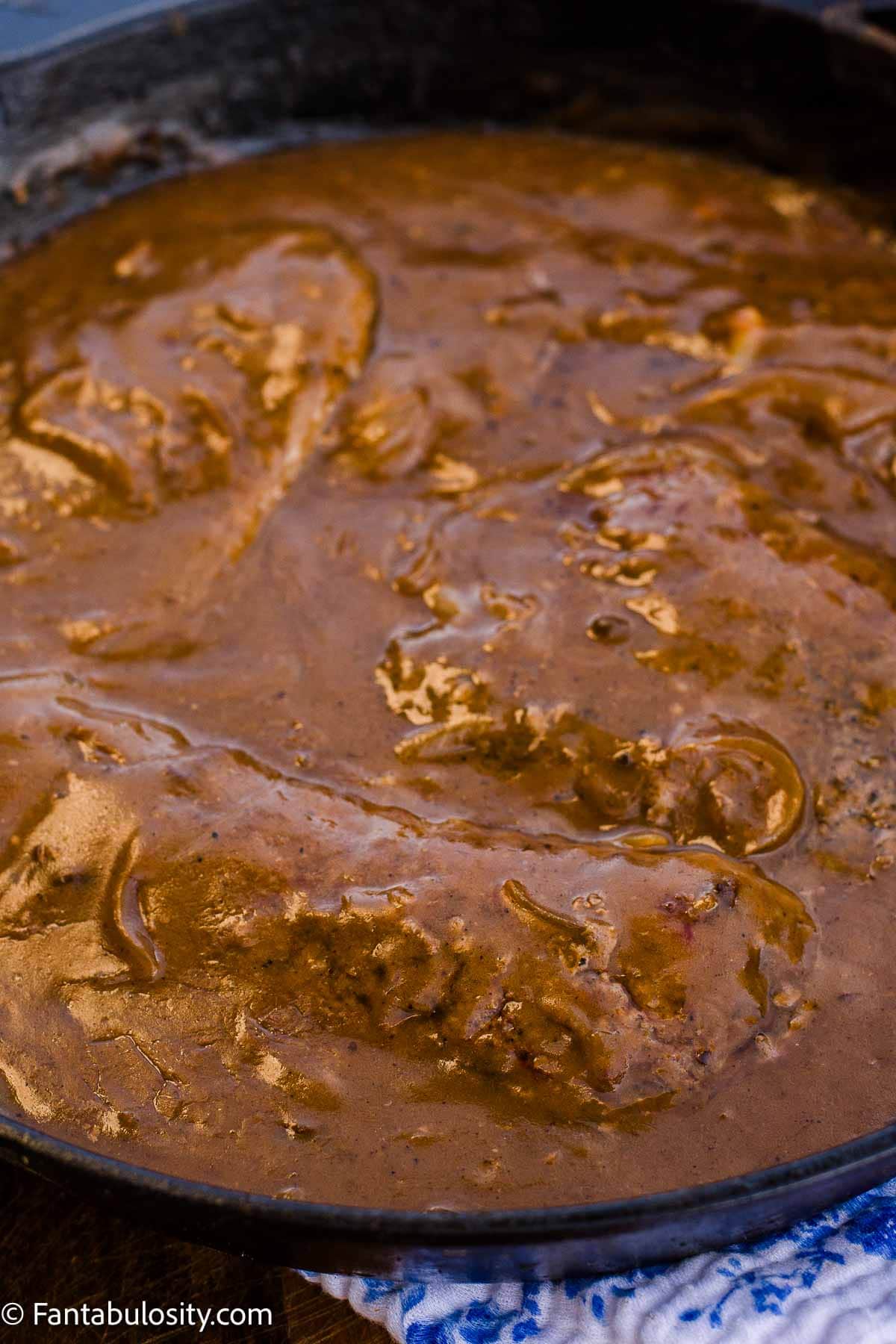 Cube steaks covered with onion gravy in a cast-iron skillet.