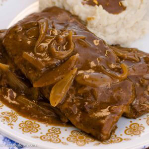 Smothered cube steak topped with onion gravy beside mashed potatoes.