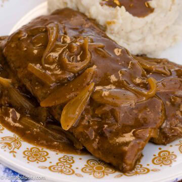 Smothered cube steak topped with onion gravy beside mashed potatoes.
