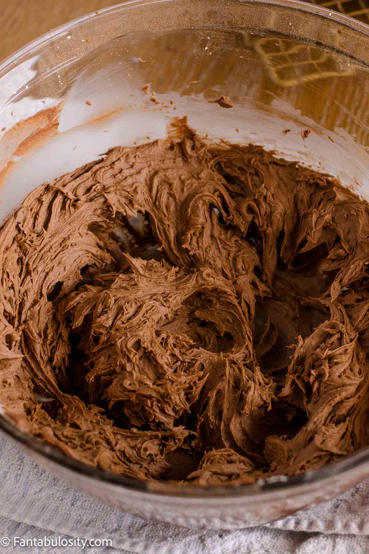 Whipped chocolate buttercream frosting in a glass mixing bowl.