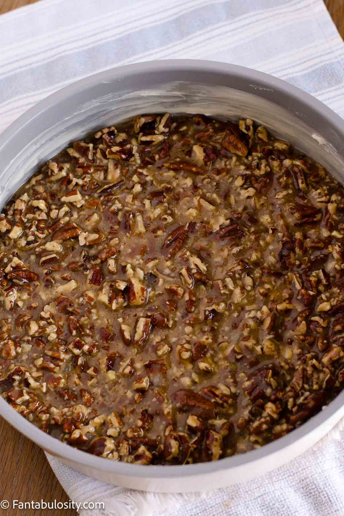 Pecan topping spread in the bottom of a round metal cake pan