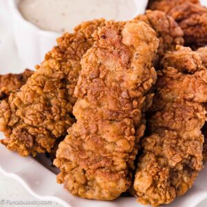 Crispy fried steak fingers piled on a plate beside white gravy.