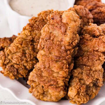 Crispy fried steak fingers piled on a plate beside white gravy.