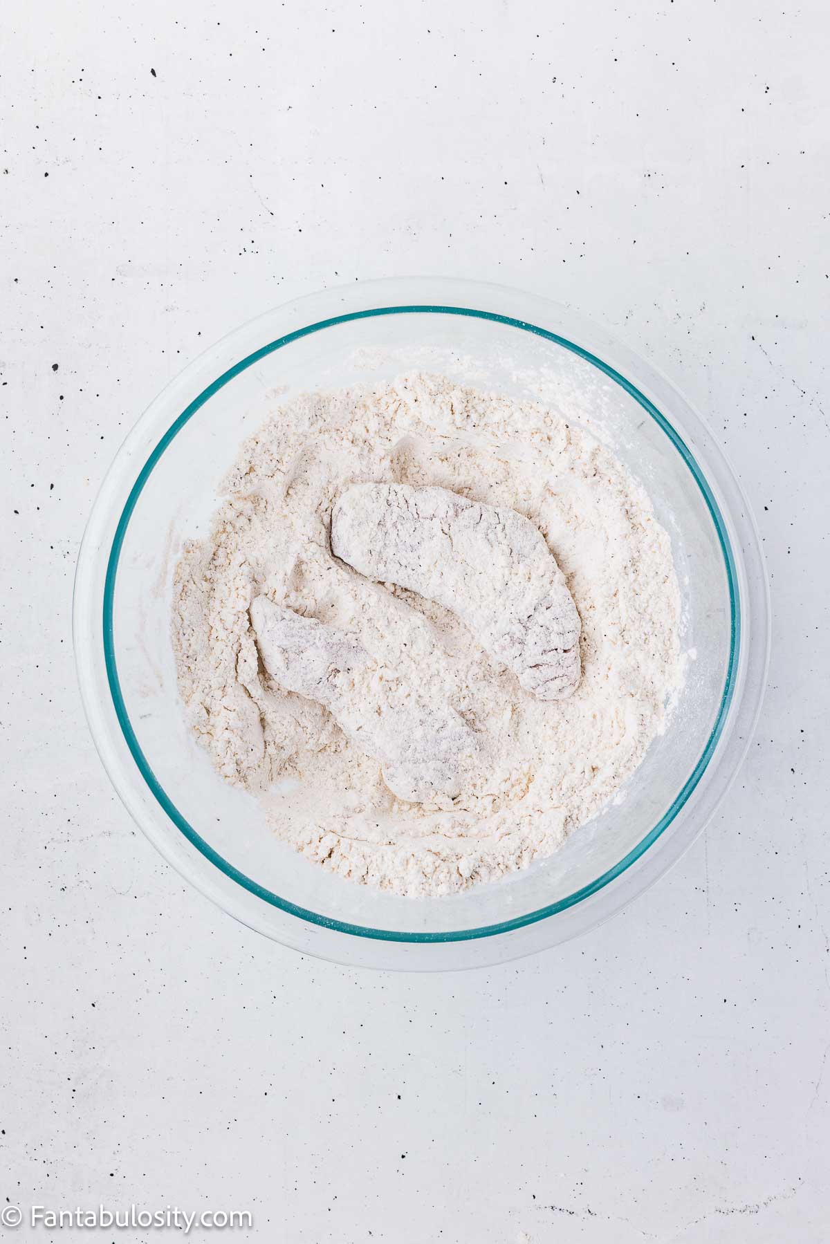 Steak strips covered in the first layer of seasoned flour.