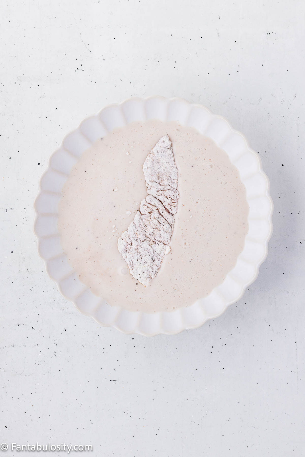 A flour-coated steak strip dipped back into the buttermilk marinade.