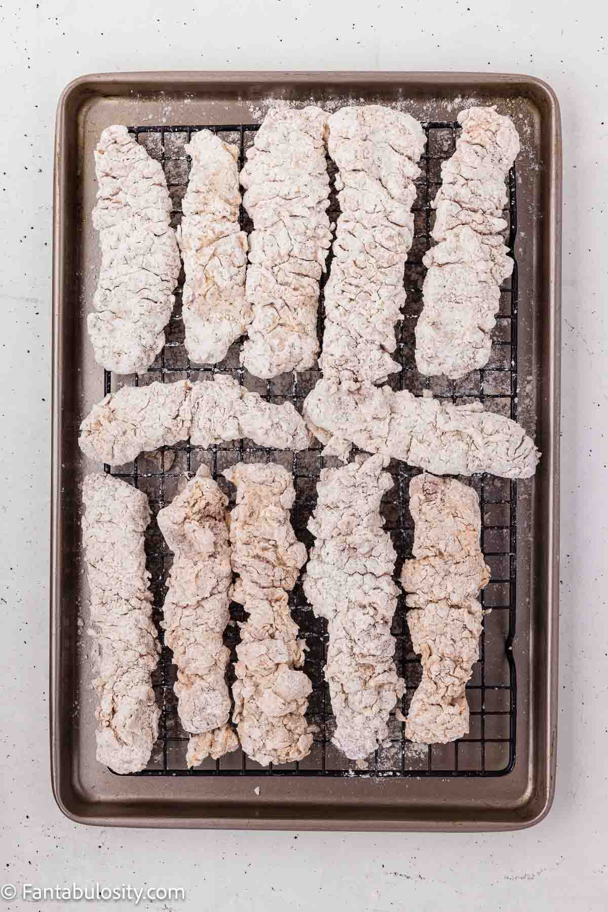 Breaded steak fingers resting on a wire rack before frying.