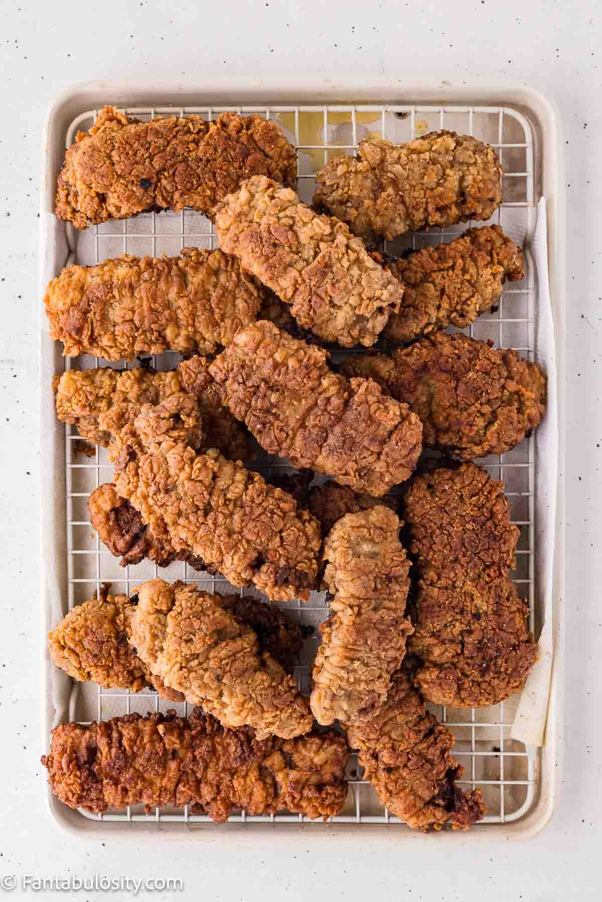 Fried steak fingers draining on a wire rack over a baking sheet.