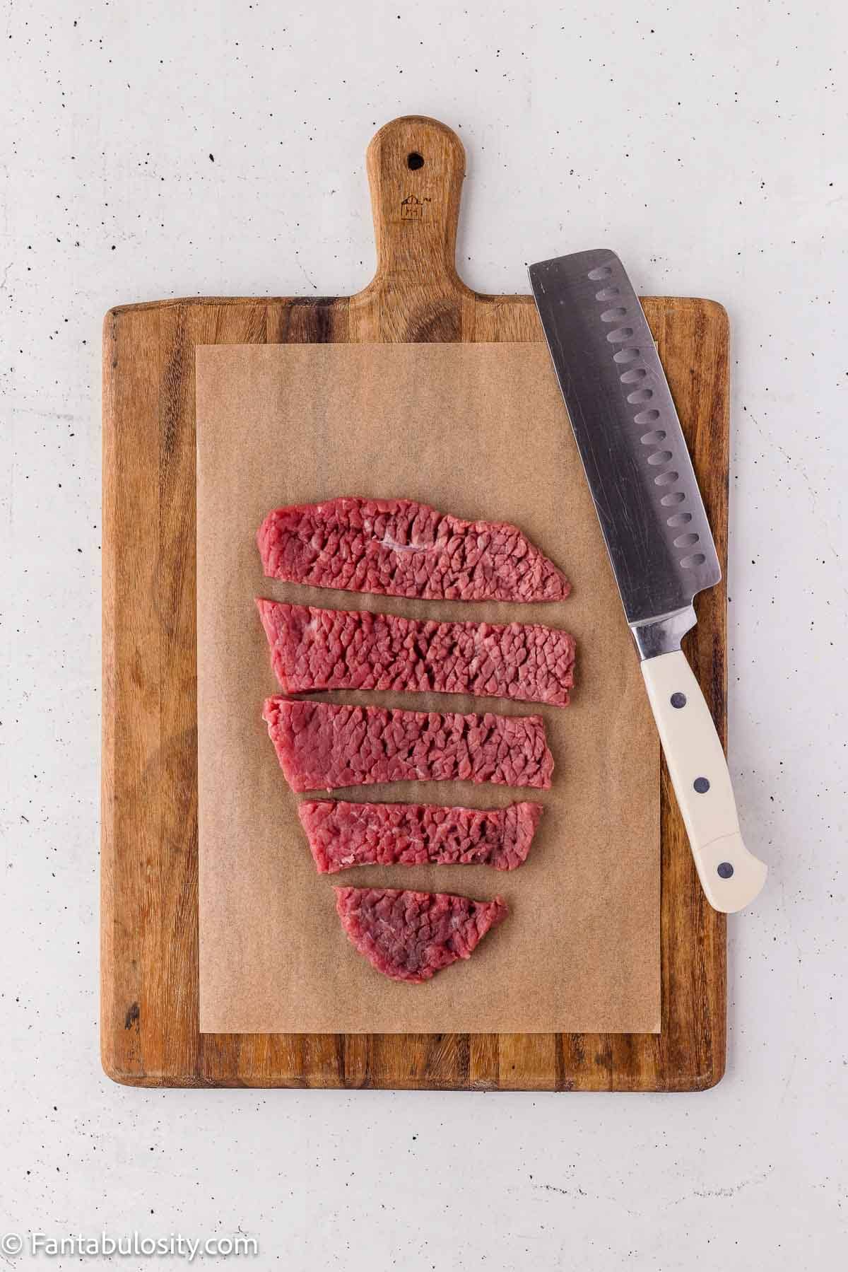 Cube steak cut into strips on a wooden cutting board.