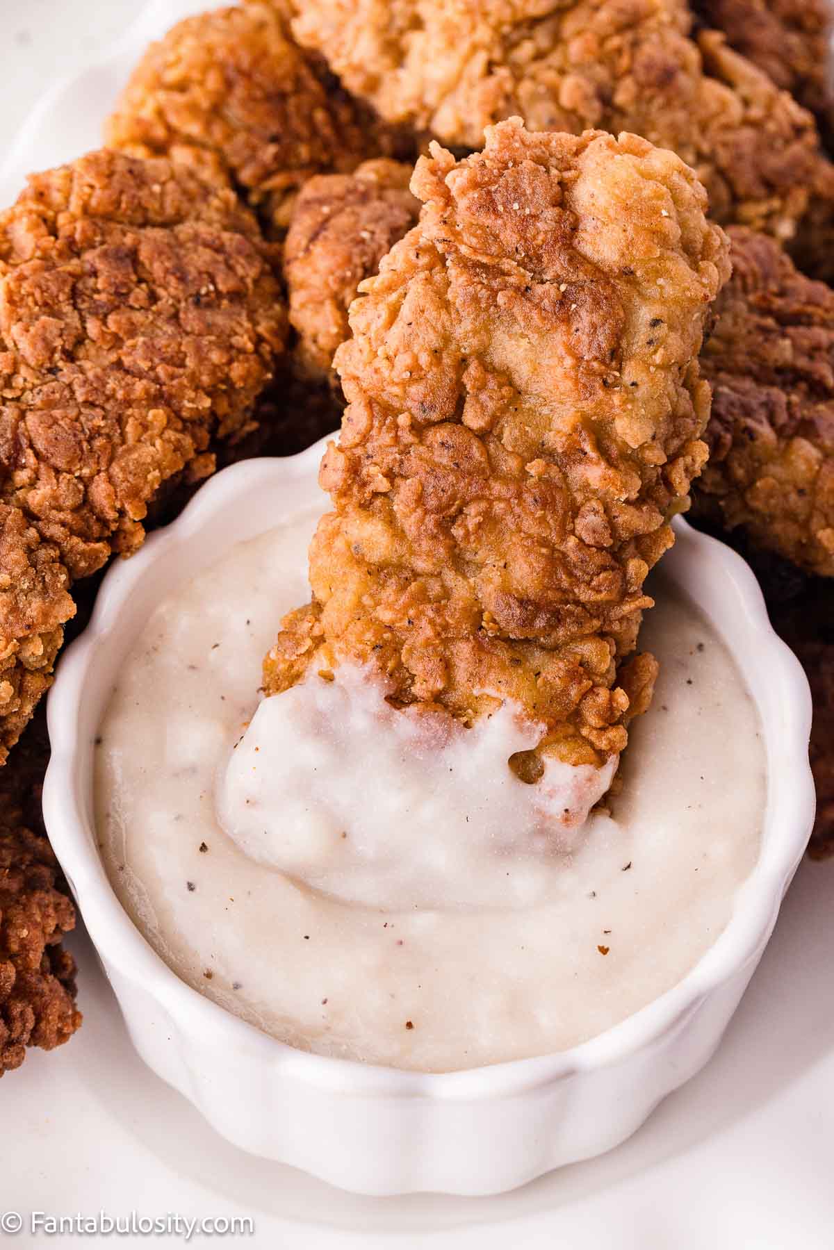 A fried steak finger dipped into a bowl of white gravy.