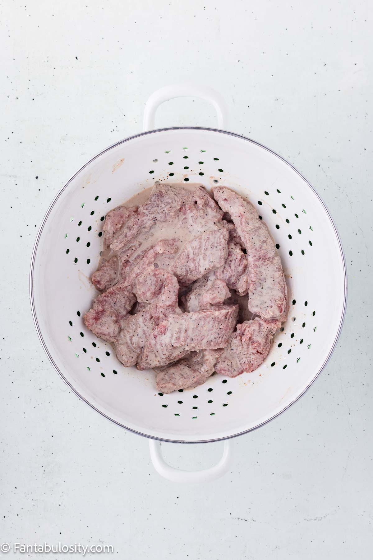 Marinated cube steak strips draining in a colander.