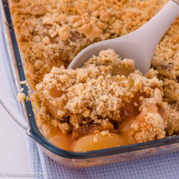 Apple crumble without oats with golden crumbs and apple filling on a serving spoon in a glass baking dish.