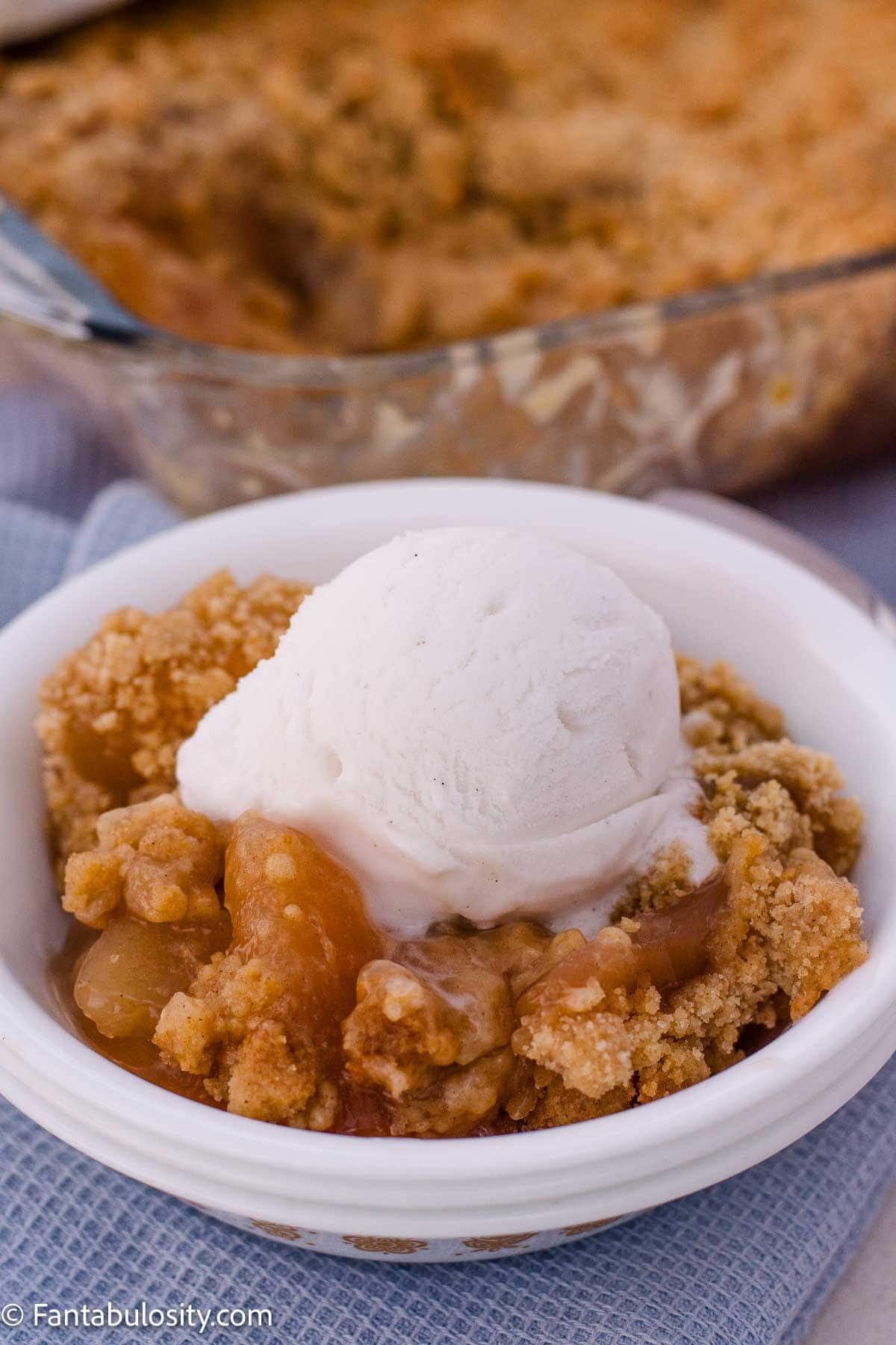 A bowl of apple crumble topped with a scoop of vanilla ice cream.