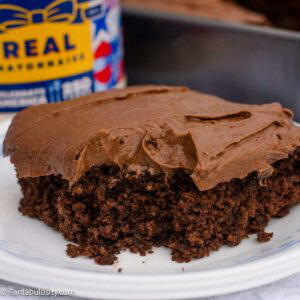 Close-up slice of chocolate mayonnaise cake with thick chocolate buttercream and a jar of mayonnaise behind it.