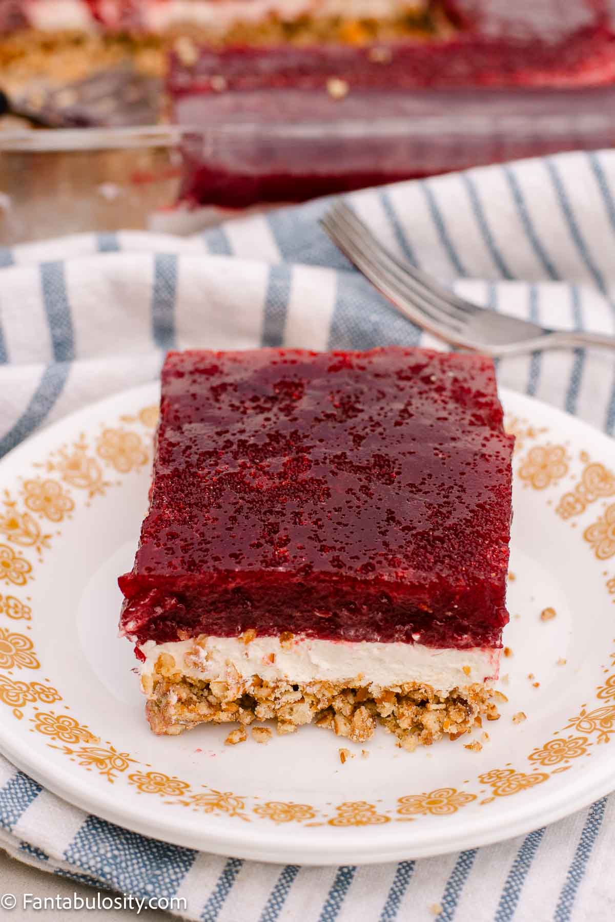 A slice of cranberry pretzel salad with red cranberry topping, white cream cheese filling, and a coarse pretzel crust.