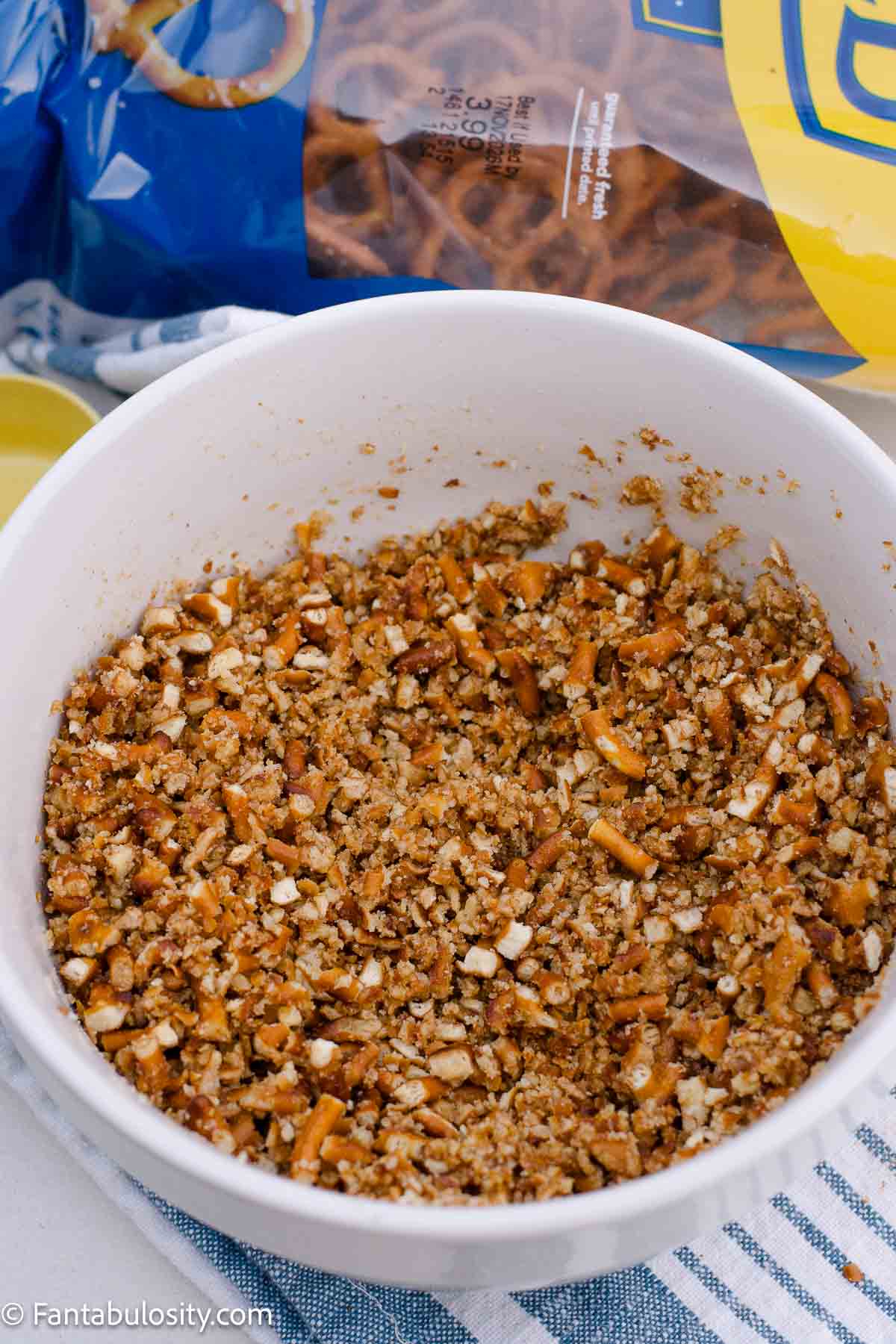 Coarsely crushed pretzels mixed with melted butter and sugar in a white bowl.