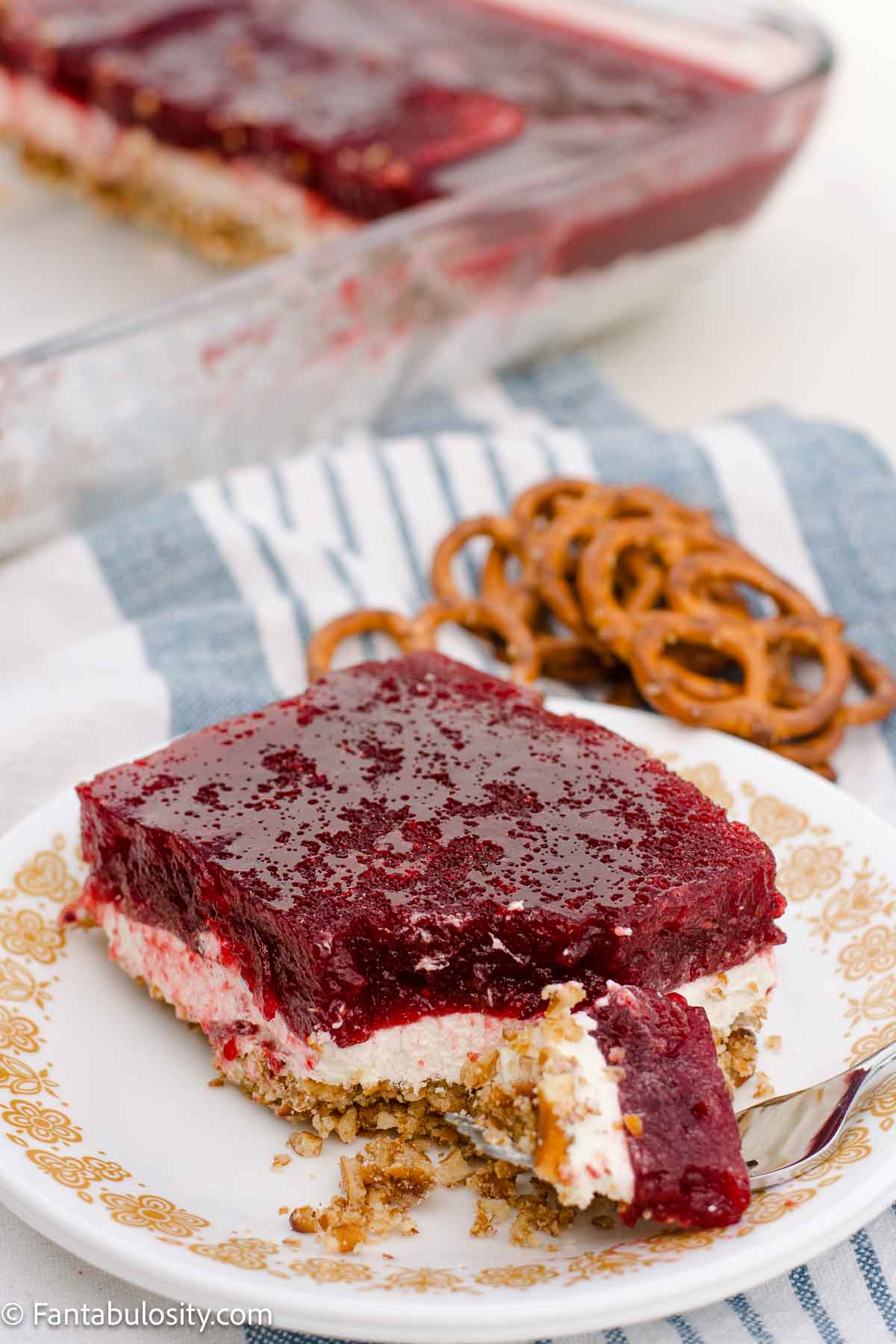 A plated slice of cranberry pretzel salad with a forkful and loose pretzel crumbs.