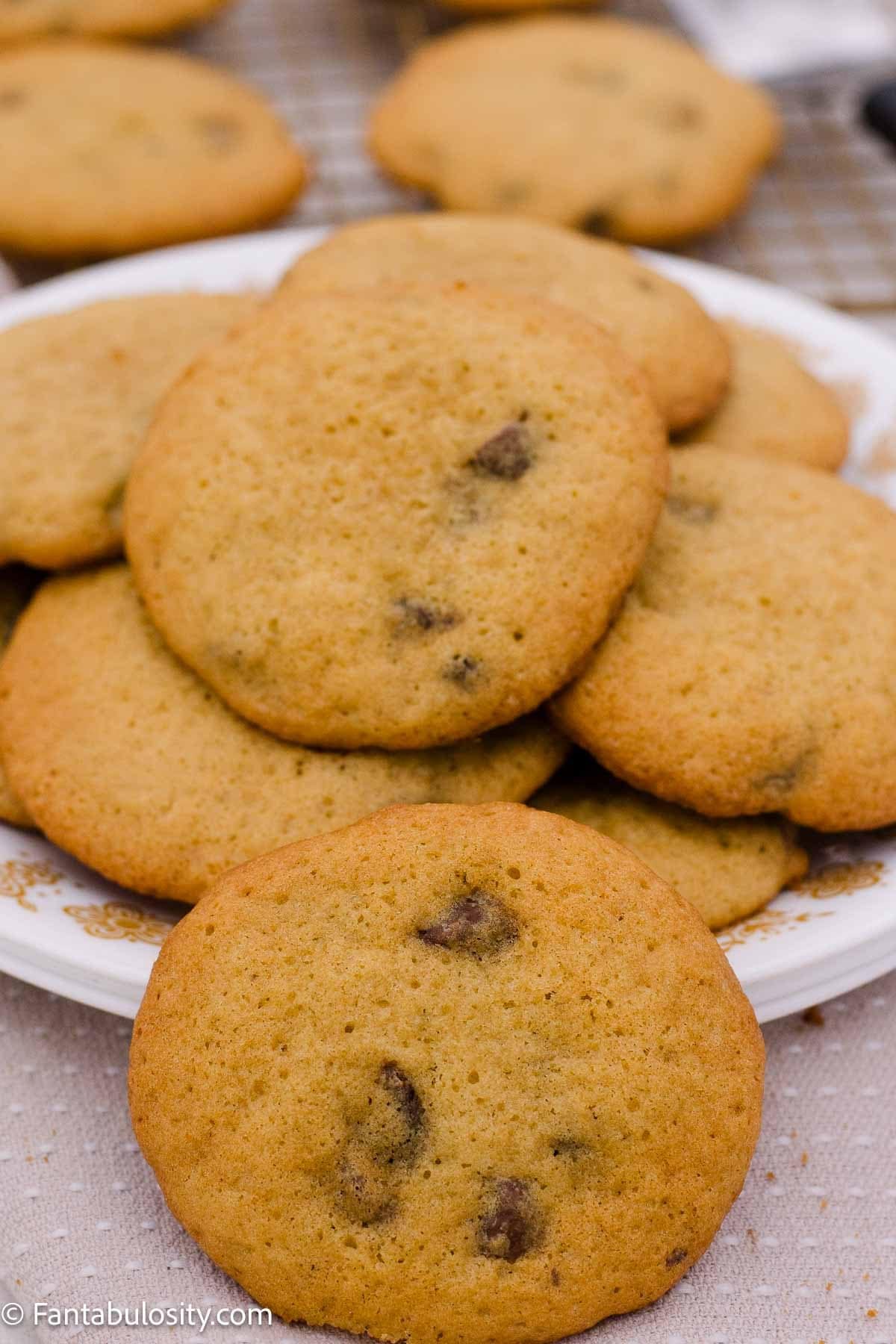 A chocolate chip cookie in front of a plate piled with more cookies.