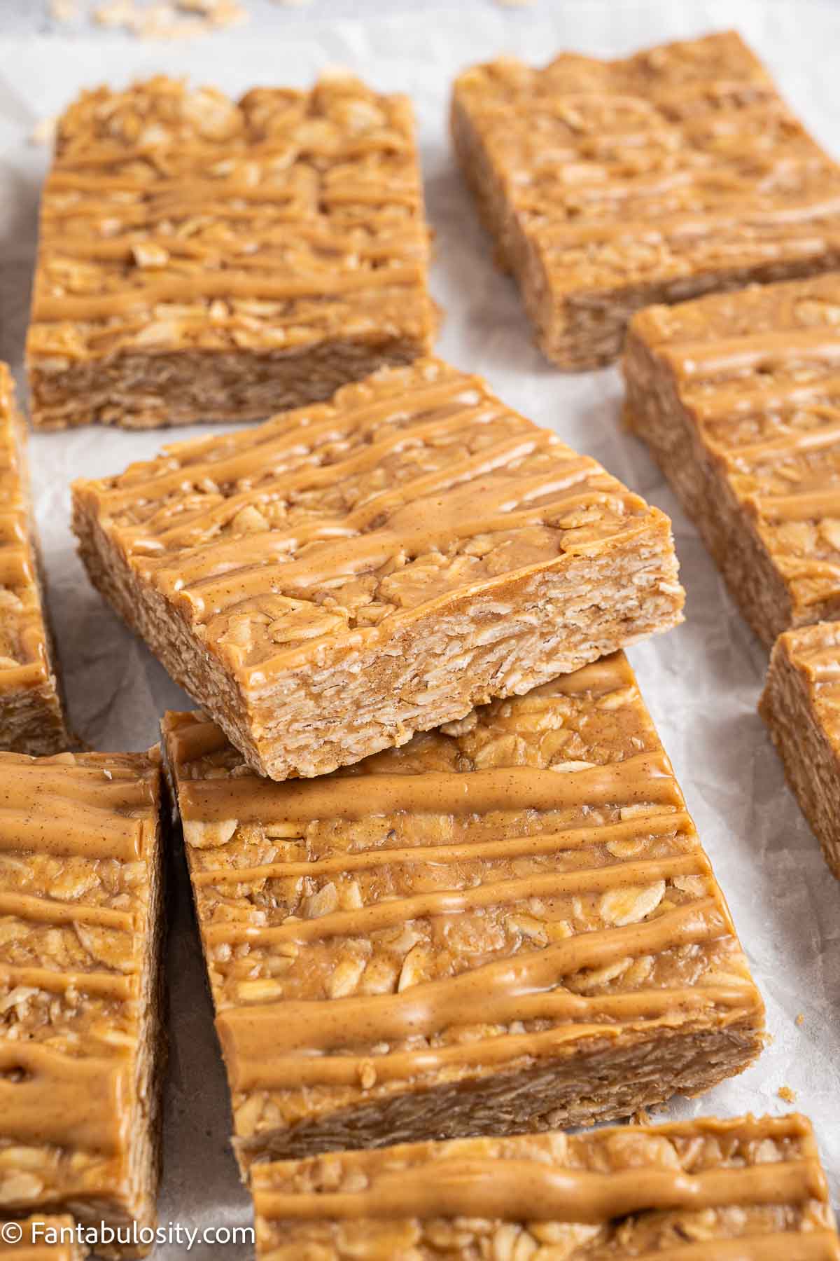 Peanut butter oatmeal bars topped with peanut butter drizzle on parchment paper.