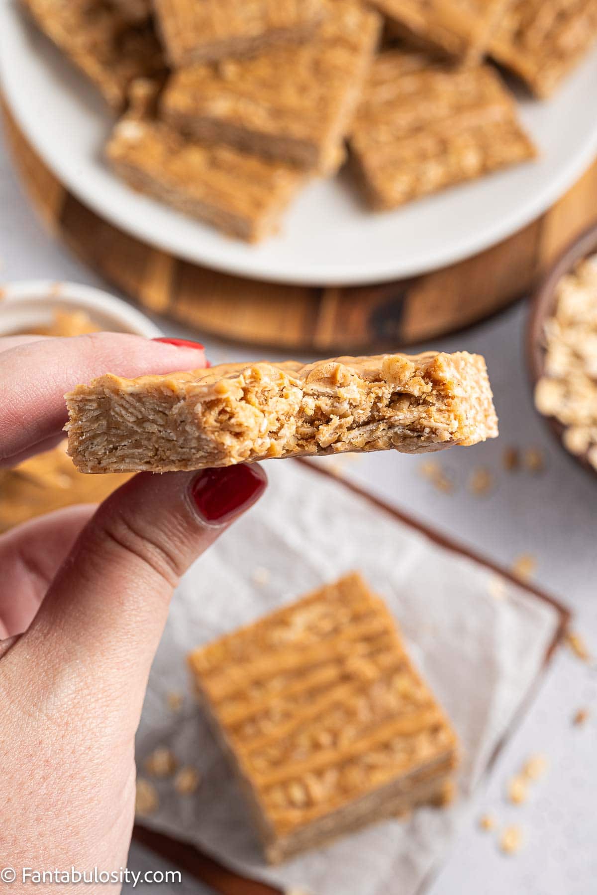 A hand holding a peanut butter oatmeal bar to show its chewy oat texture.
